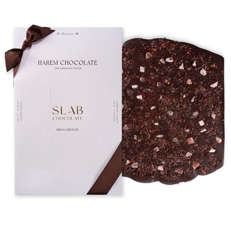 Rich dark chocolate with crushed toppings on a black background, paired with elegant white packaging featuring brown ribbon accents. Perfect for gourmet chocolate lovers.