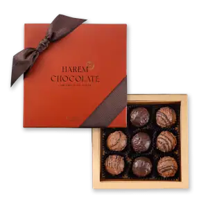Rich, assorted chocolate truffles in a luxurious gold gift box with a brown ribbon, perfect for gifting or indulging.