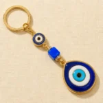 Gold-tone evil eye keychain with blue glass cube bead on dark surface