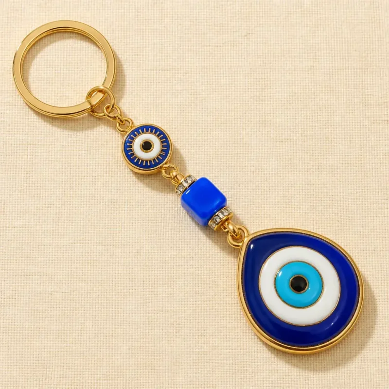 Gold-tone evil eye keychain with blue glass cube bead on dark surface