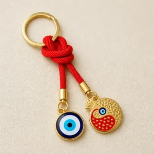 Evil eye pomegranate keychain gold charms and red cord on dark background