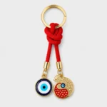 Evil eye pomegranate keychain with red cord held in palm