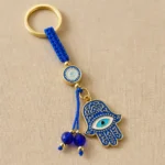 Hamsa evil eye keychain with blue beads on dark textured surface